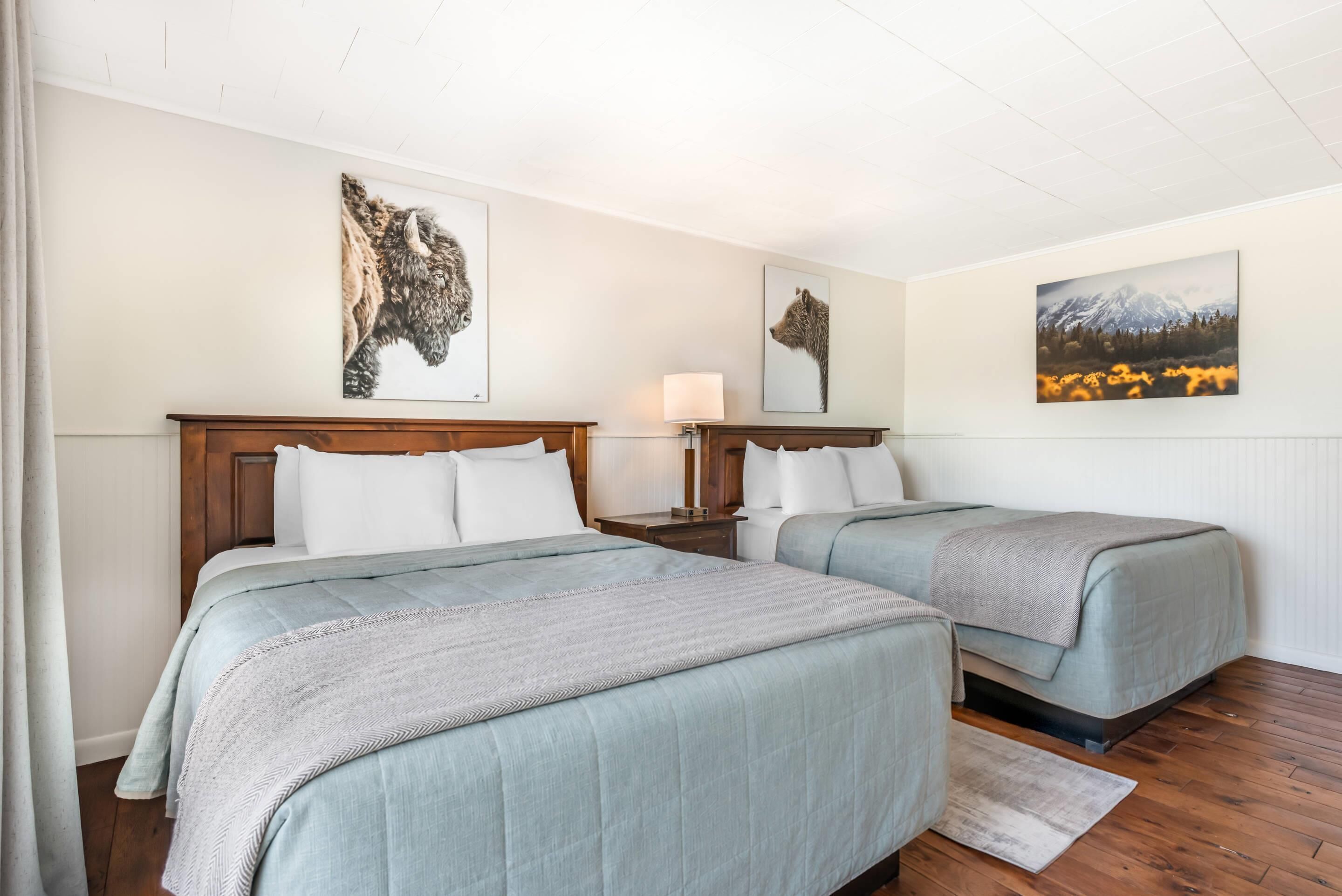Ein Hotelzimmer mit zwei Betten, jeweils mit Kopfteil, Nachttisch, Lampe und einem Bild an der Wand.