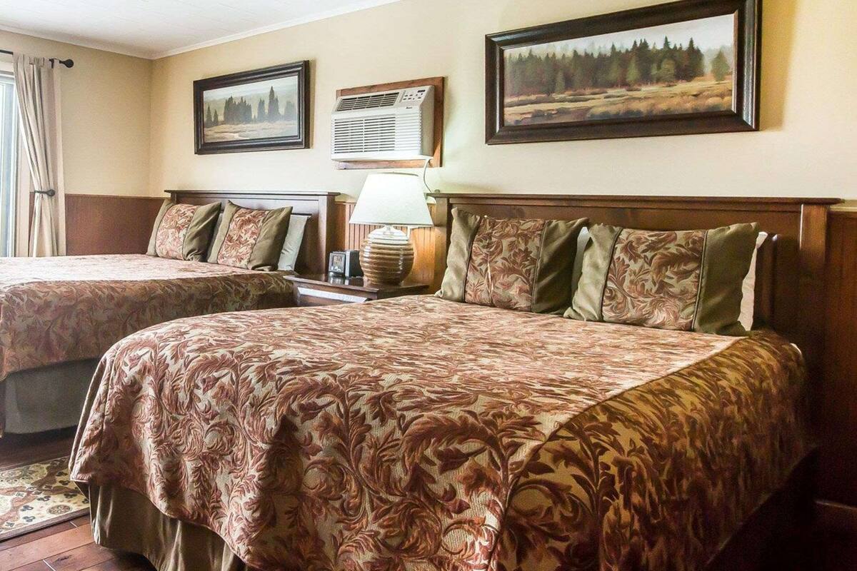 A hotel room with two beds, a nightstand with a lamp, and two framed pictures on the wall.