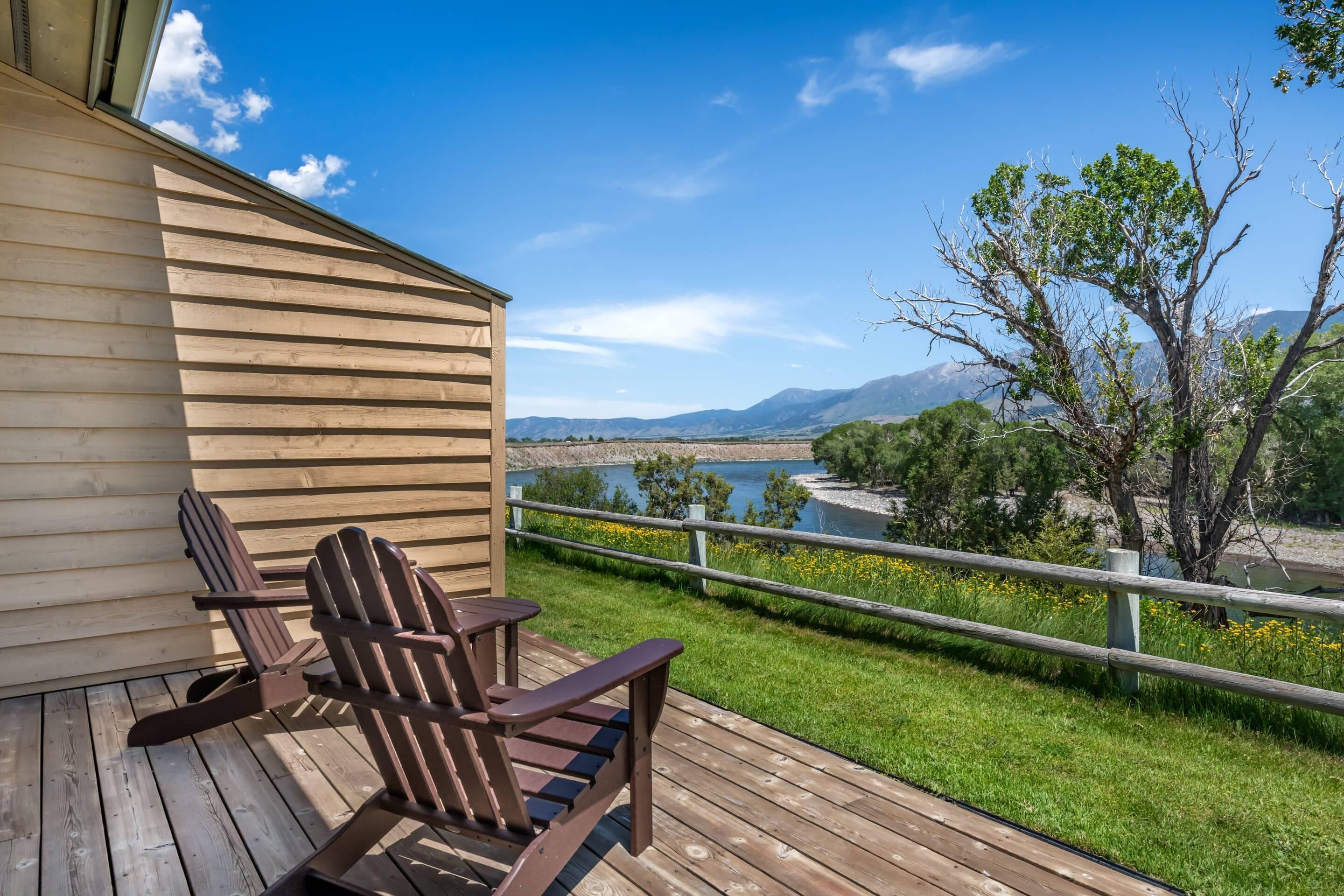 A wooden deck with Adirondack chairs, overlooking a river and mountains.