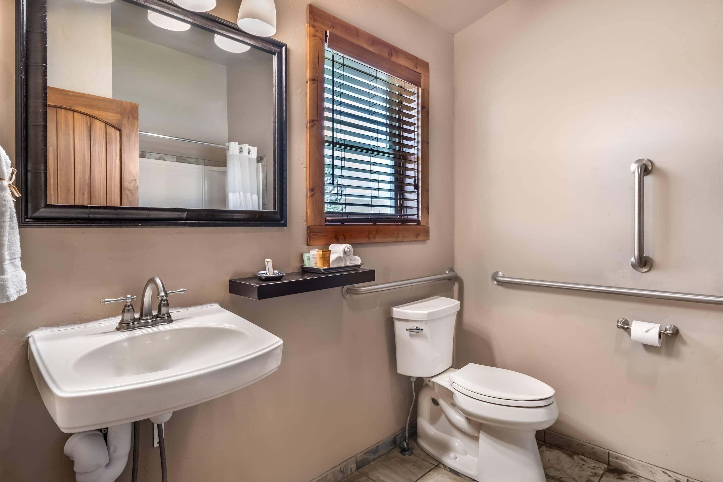 A bathroom with a sink, toilet, and a window with blinds.
