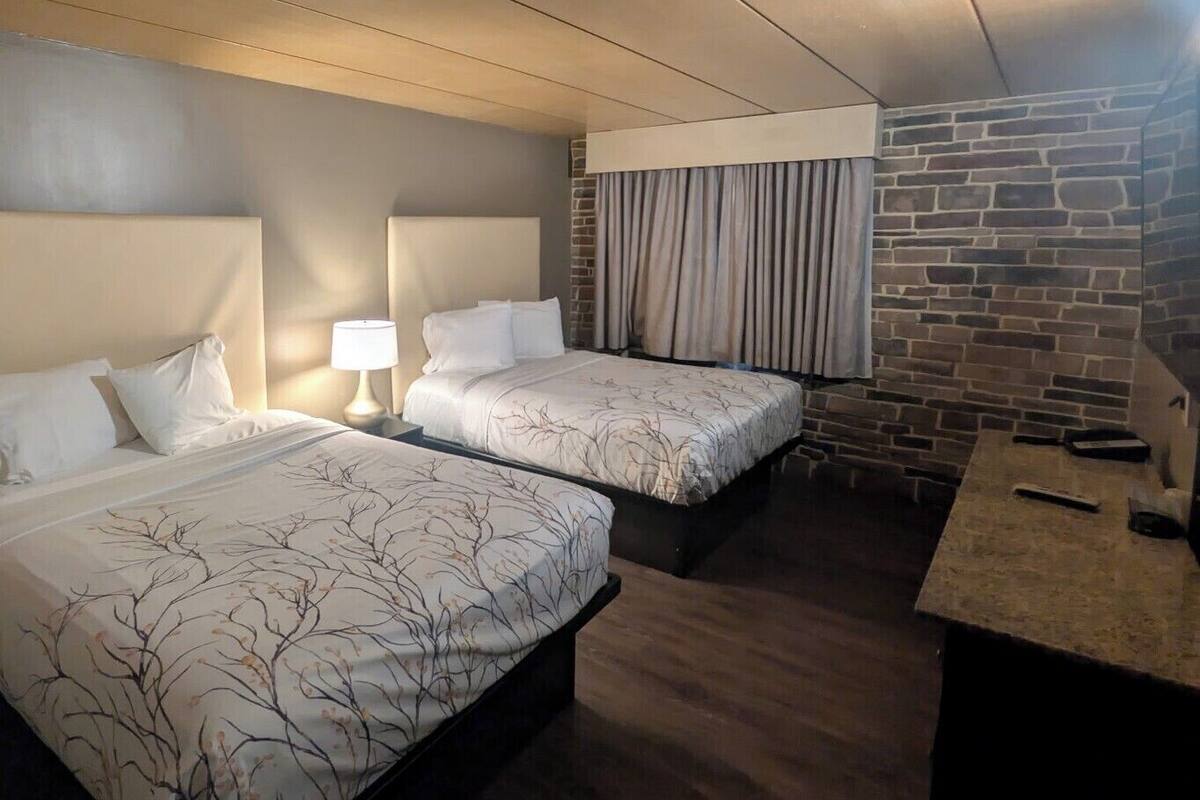 A hotel room with two beds, a stone accent wall, a desk, and a window with curtains.