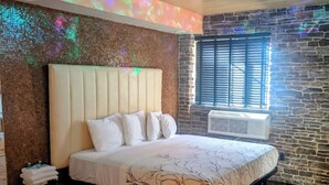 A modern bedroom with a large bed, a headboard, and a window with blinds. - Surfside Motel (Howard Beach)