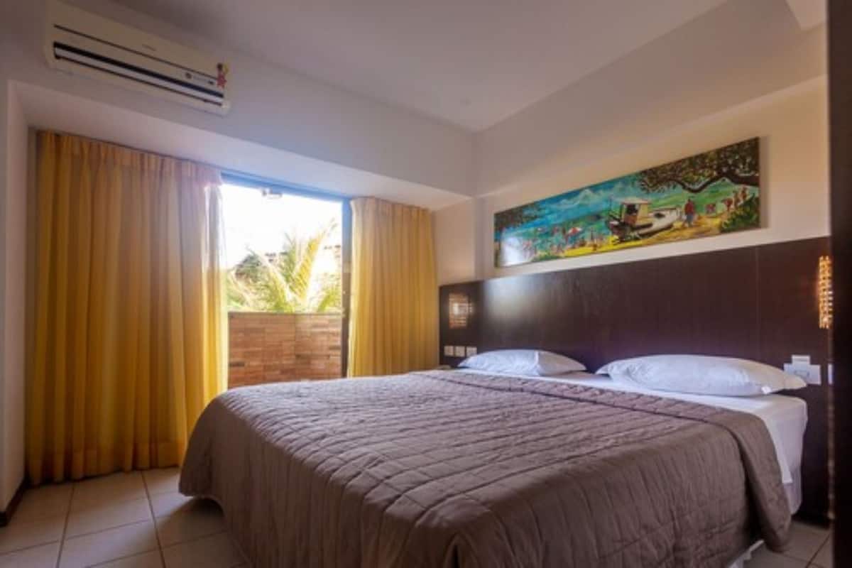 A hotel room with a large bed, a painting on the wall, and a window with curtains.