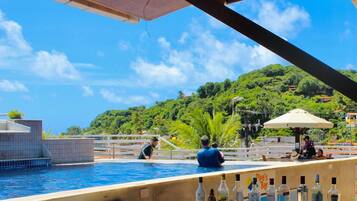 Um bar à beira da piscina com vista para uma encosta verdejante.