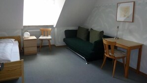 A small, well-lit room with a sloped ceiling, a bed, a desk, a chair, and a green sofa. - Landgasthof Wellmann (Markt Taschendorf)