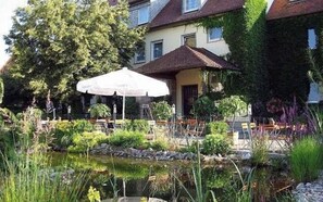 A garden with a pond, outdoor seating, and a building with a tiled roof. - Landgasthof Wellmann (Markt Taschendorf)