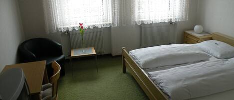 Una habitación de hotel con una cama, un escritorio con silla, un radiador y una ventana con cortinas.
