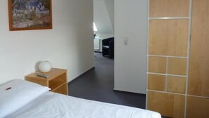 A hotel room with a bed, a bedside table with a lamp, a wooden wardrobe, and a painting on the wall. - Landgasthof Wellmann (Markt Taschendorf)