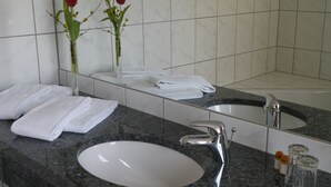 A bathroom with a large mirror, two sinks, and a vase with red flowers. - Landgasthof Wellmann (Markt Taschendorf)