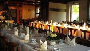 A long dining table set with candles, plates, and cutlery in a room with wooden furniture and a window. - Landgasthof Wellmann (Markt Taschendorf)