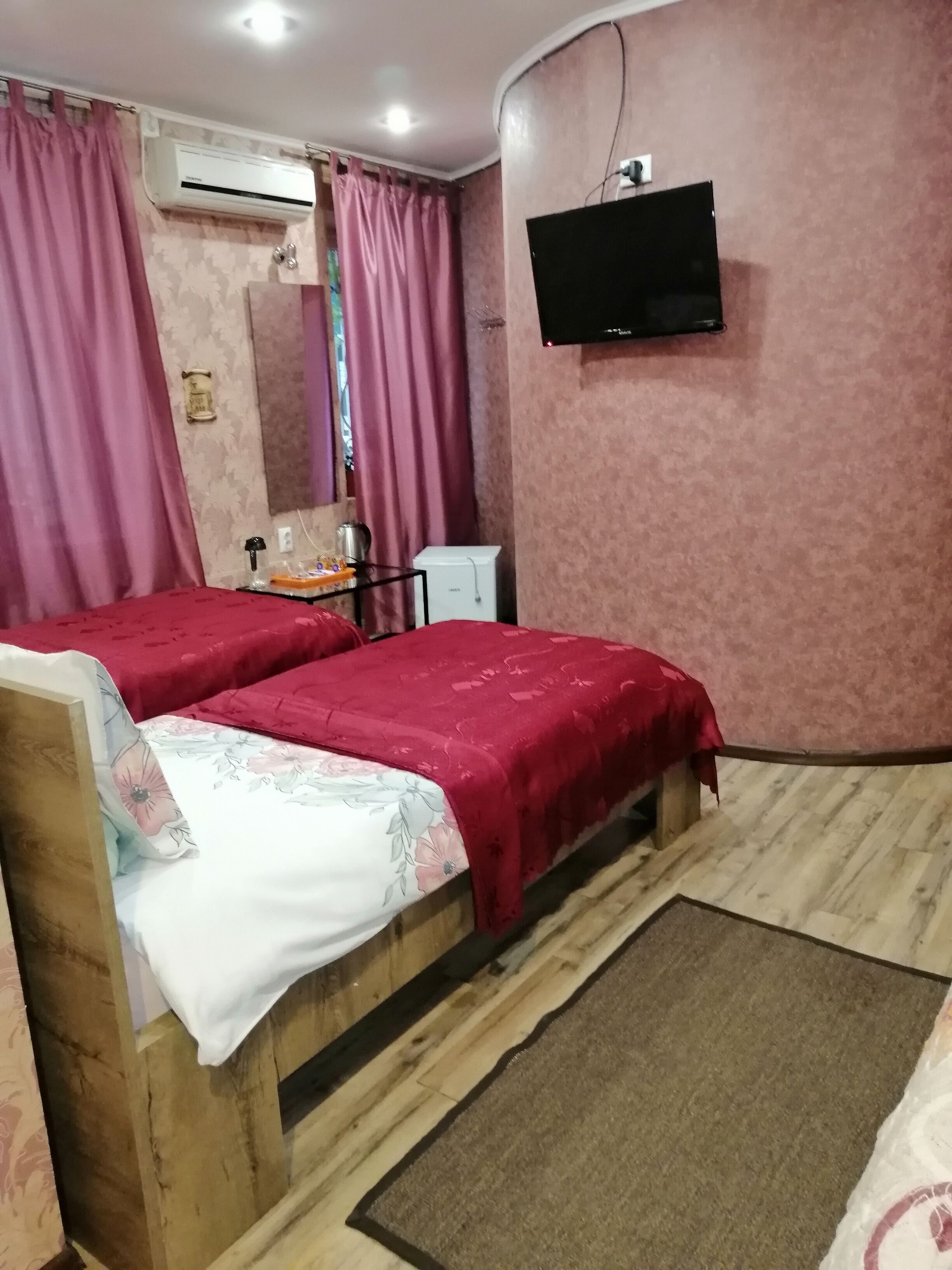 A room with two wooden beds, a TV mounted on the wall, an air conditioner, and a small white cabinet.