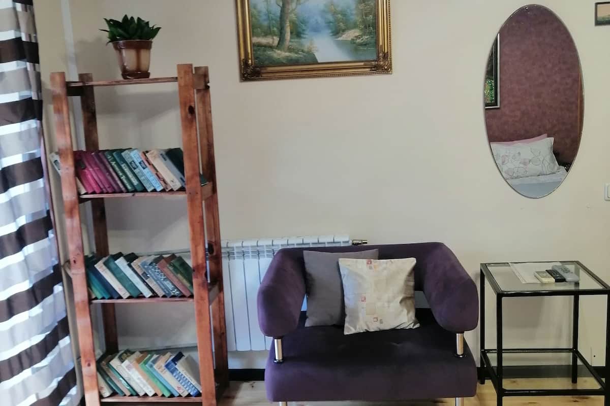 A living room with a purple sofa, a wooden bookshelf, a painting, a mirror, and a small table.