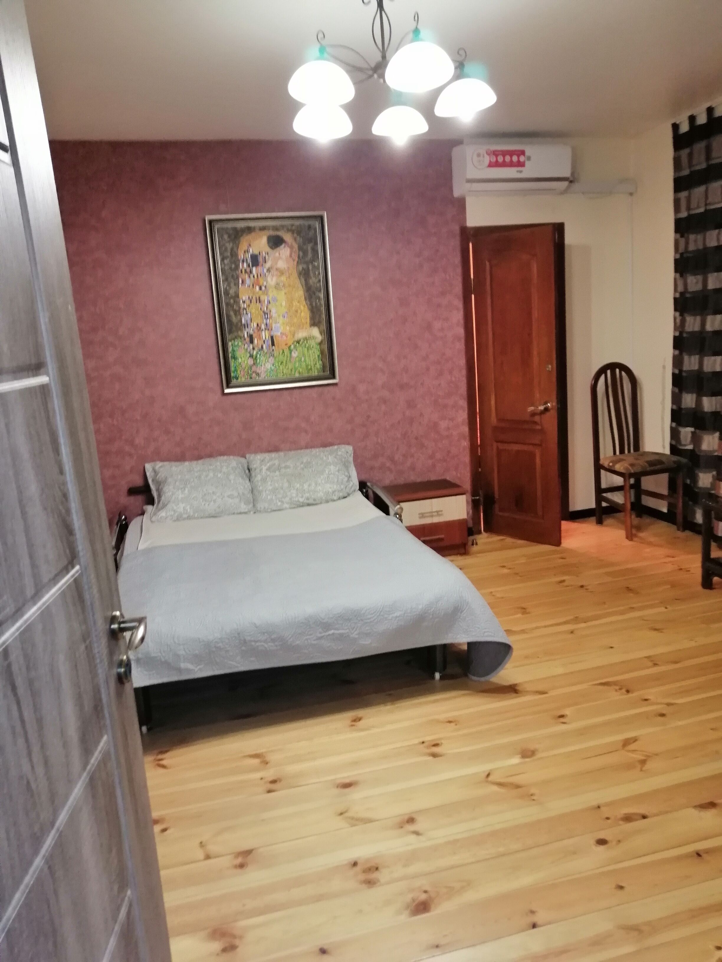 Un dormitorio con cama, una silla, un cuadro en la pared y un equipo de aire acondicionado.