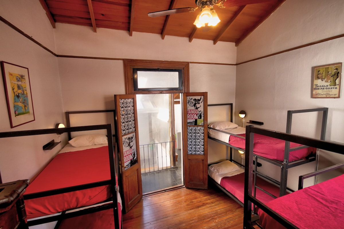 A dormitory room with bunk beds, wooden beams on the ceiling, and a door with a poster.