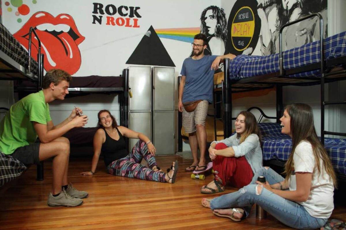 A dormitory room with bunk beds, a kitchenette, and a wall with a Rolling Stones logo.