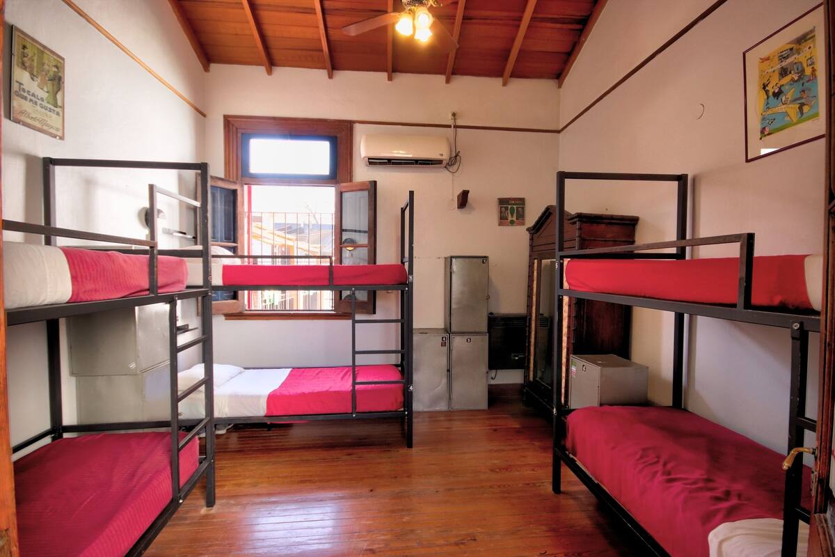 A dormitory room with bunk beds, wooden floors, a ceiling fan, and a window.