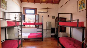 Un dormitorio con literas, piso de madera, ventilador de techo y ventana.