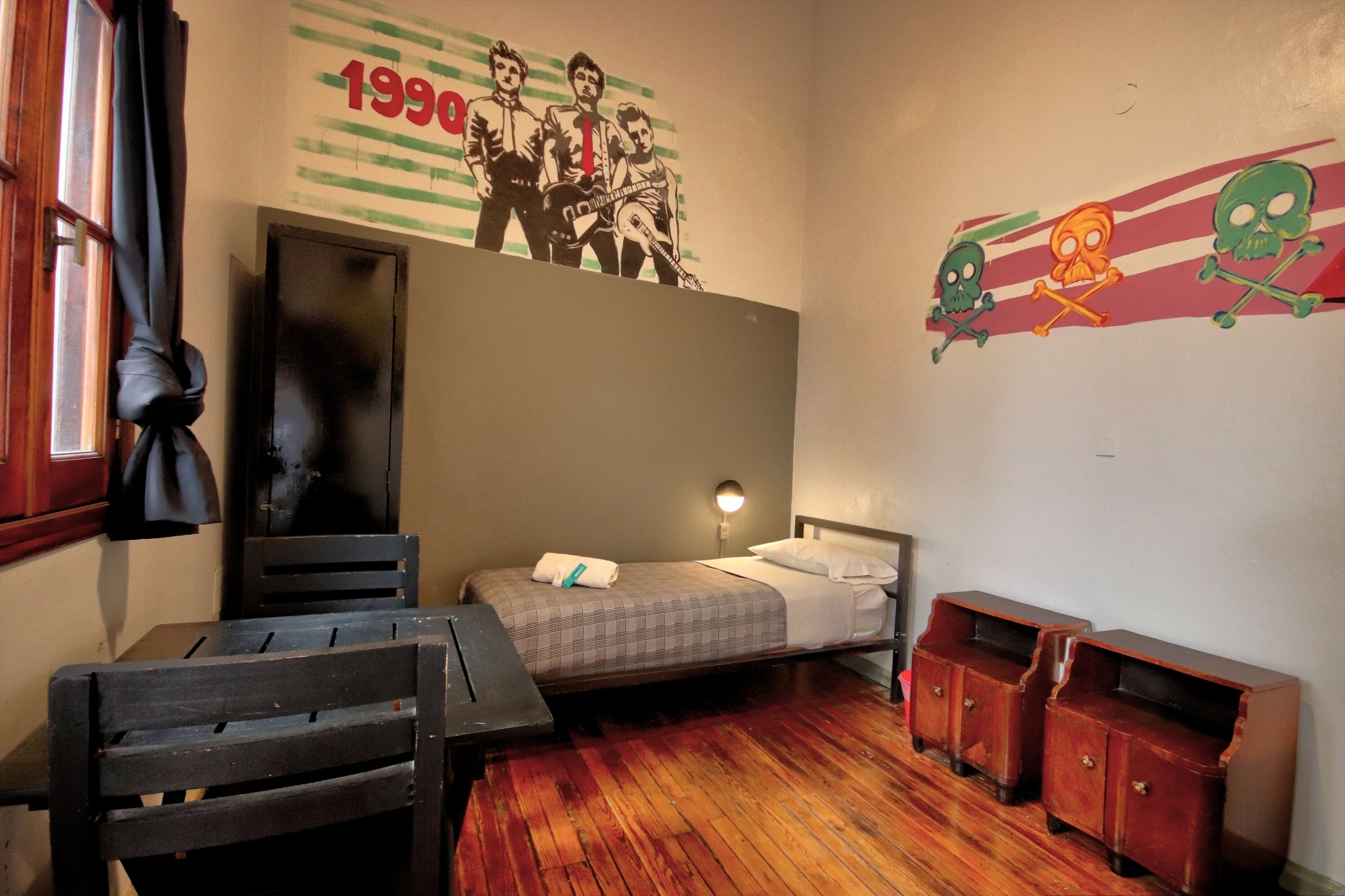 A small room with a bed, a desk, and a chair. There is a wall decoration and a small cabinet.