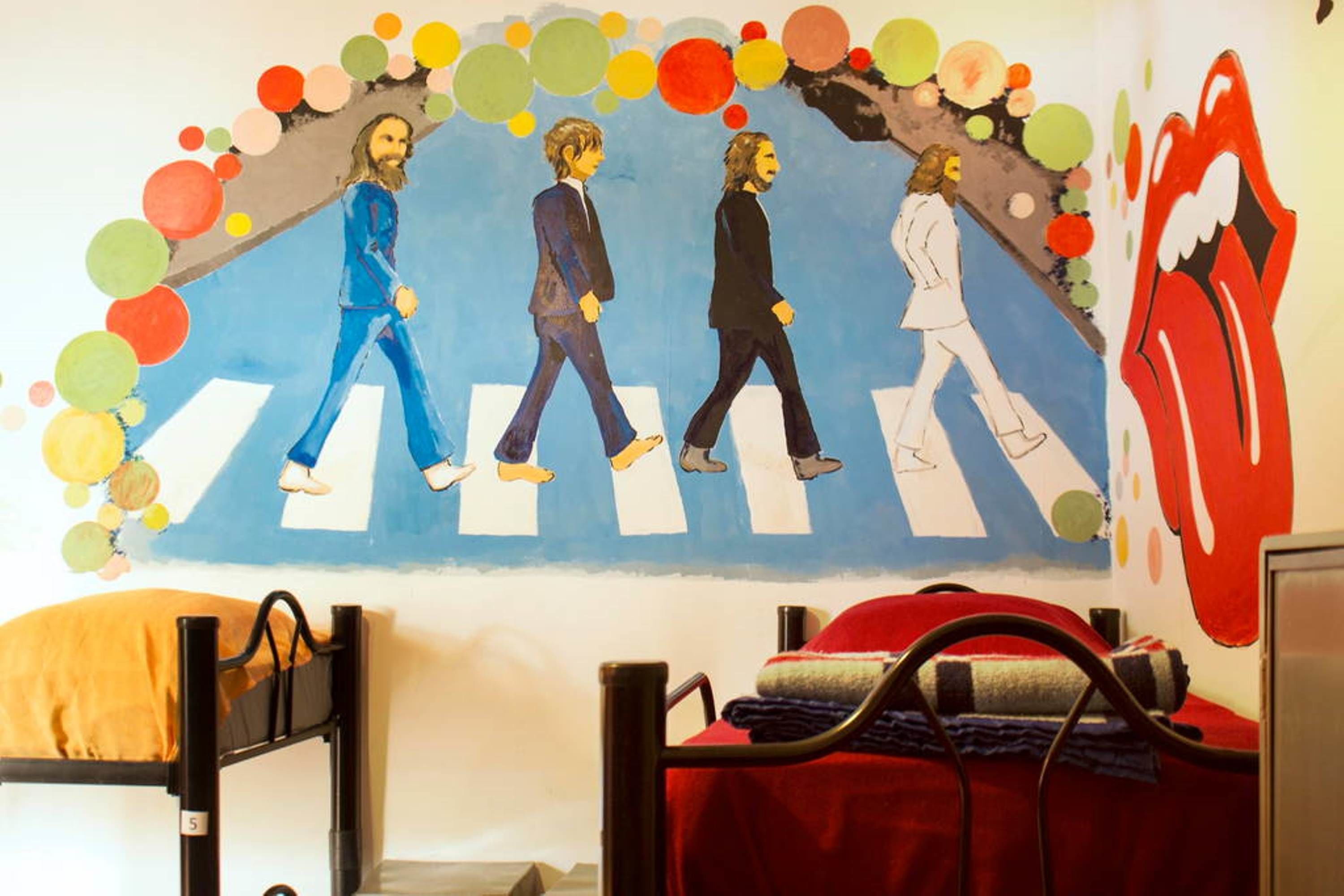 Une chambre avec des lits superposés, une fresque représentant les Beatles traversant un passage piéton, et une couverture rouge et blanche à rayures sur l’un des lits.