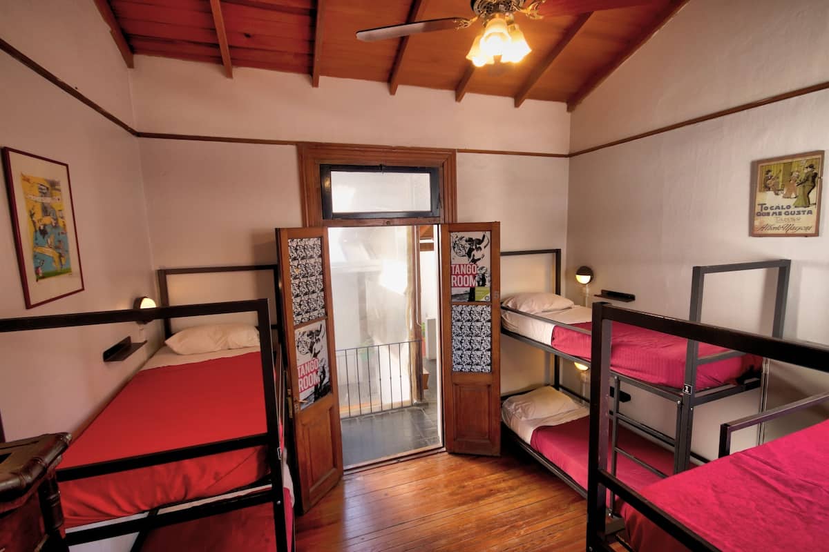 A dormitory room with bunk beds, wooden beams on the ceiling, and a door with a poster.