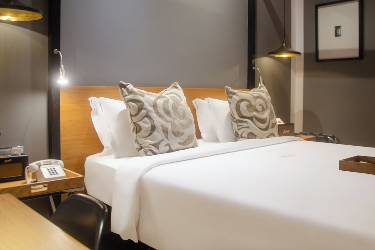 A hotel room with a bed, pillows, bedside tables, a telephone, and a lamp.