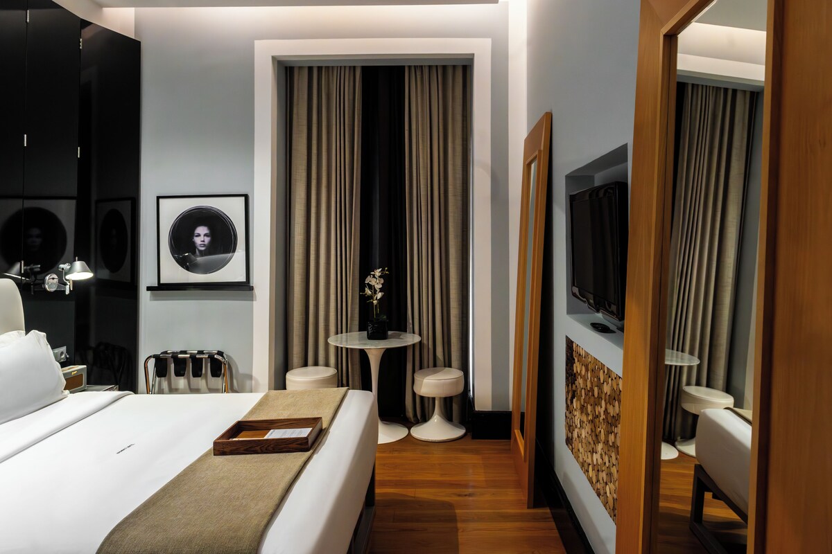 A modern hotel room with a bed, bedside tables, a TV, and a mirror.