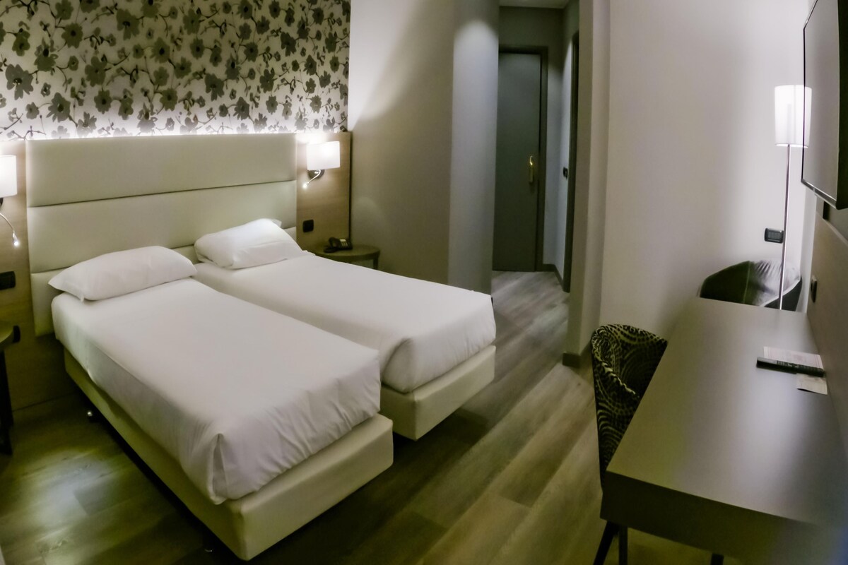 A hotel room with two beds, a desk, a chair, and a television.