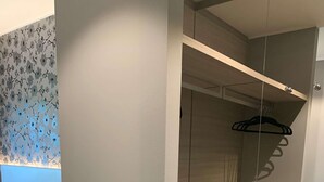 Une chambre moderne avec un lit, une armoire intégrée dotée d’un miroir et un mur orné d’un motif floral.