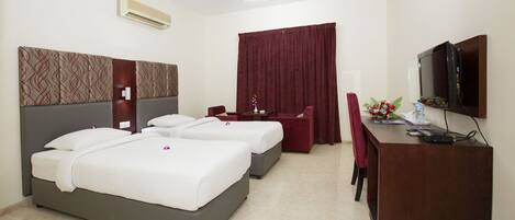 A hotel room with two beds, a desk, a chair, a TV, and a ceiling fan.