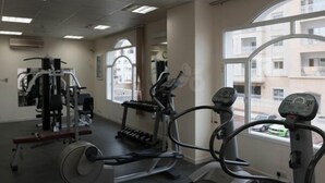A gym with cardio machines, weight equipment, and large windows offering a view of the outside. - Samara Hotel (Muscat)