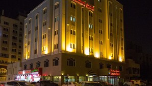 A multi-story hotel with illuminated signage, a coffee shop, and several parked cars. - Samara Hotel (Muscat)