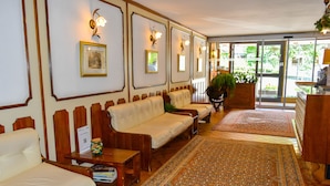 A hotel lobby with a reception desk, seating area with sofas, a patterned rug, and framed pictures on the walls. - Europa (Pinzolo)