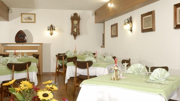 Un comedor con varias mesas dispuestas para el servicio, sillas de madera y luminarias fijadas a la pared.