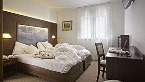 A hotel room with a wooden bed, a desk with a chair, a TV, and a painting on the wall. - Europa (Pinzolo)
