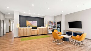 Un'accogliente area reception moderna con scrivania in legno, televisore a schermo piatto e angolo giochi per bambini con sedie arancioni e un tavolo.