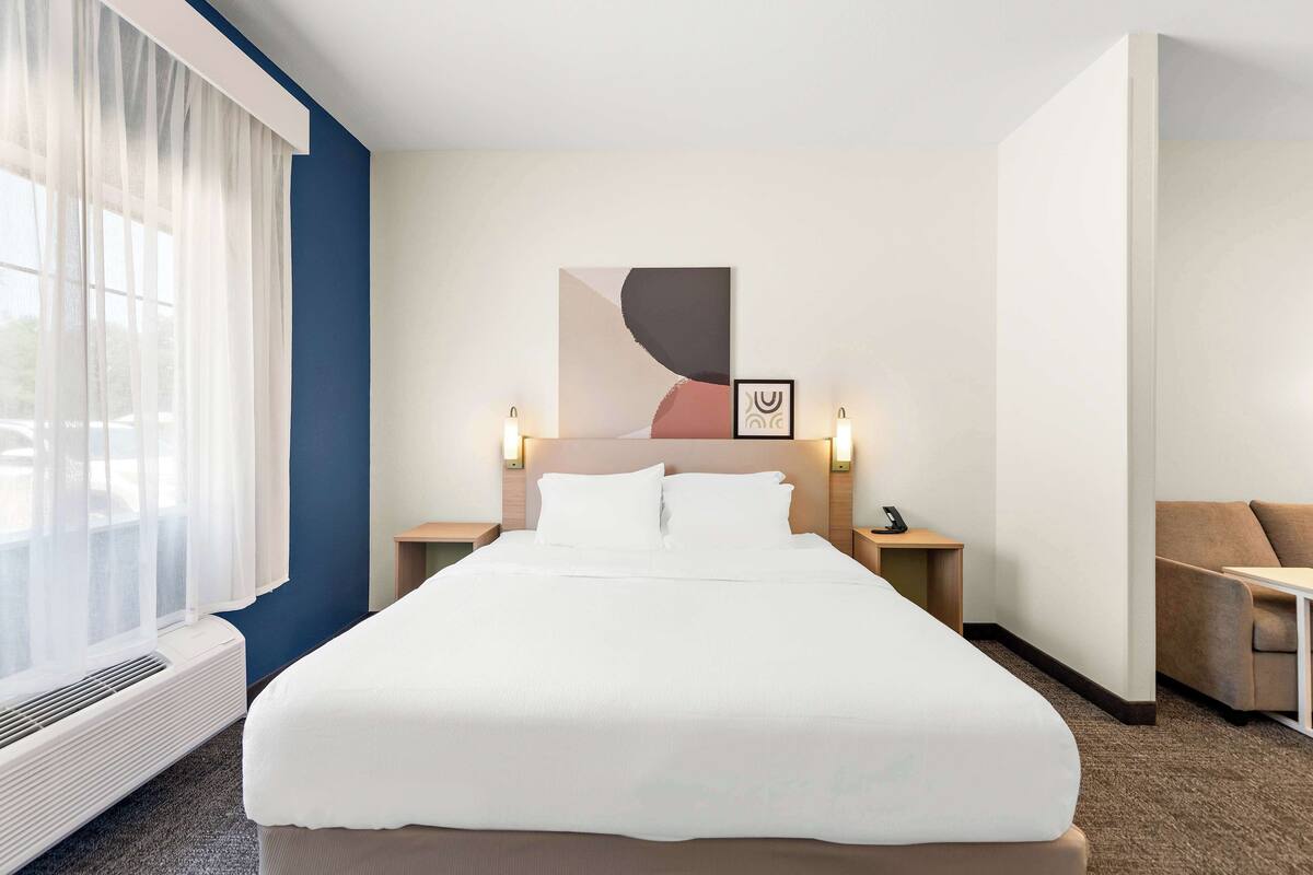 A hotel room with a large bed, bedside tables with lamps, a sofa, and a window with sheer curtains.
