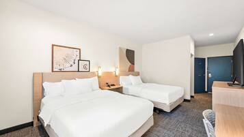 A hotel room with two beds, a desk, and a TV.