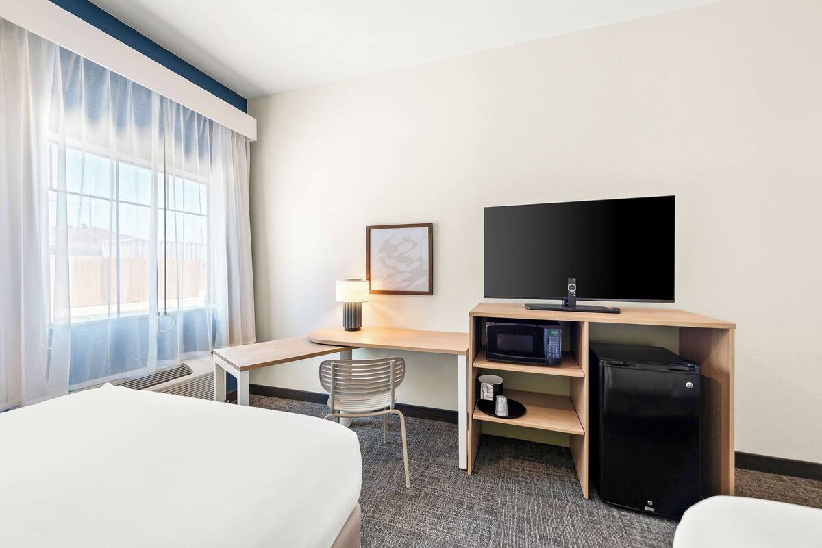 A hotel room with a bed, a desk with a television, a refrigerator, and a chair.