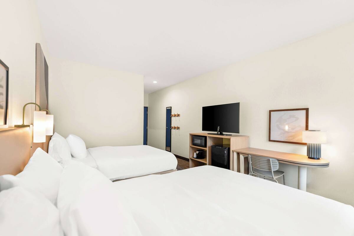 A hotel room with two beds, a desk with a chair, a TV, and a lamp.