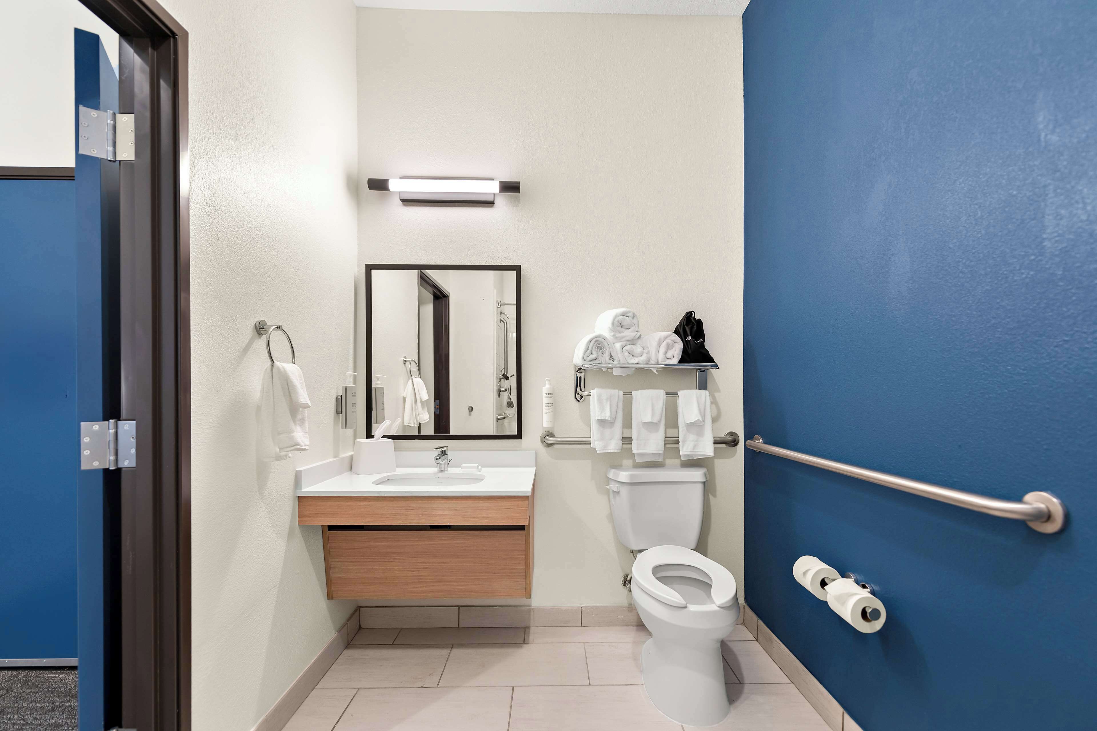 A modern bathroom with a sink, mirror, toilet, and handrails.