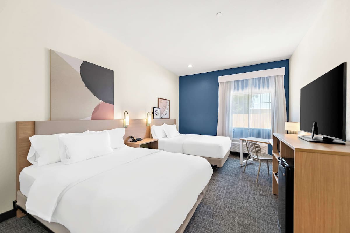 A hotel room with two beds, a desk, a chair, a television, and a large window with curtains.