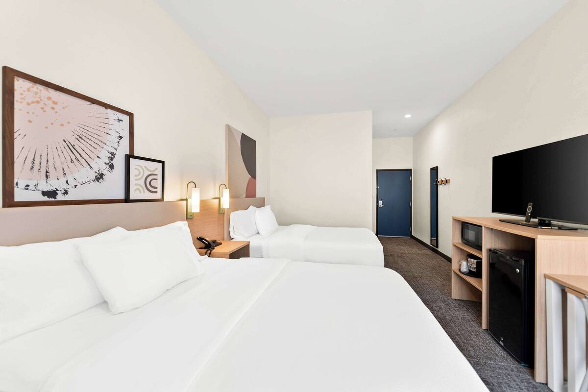 A hotel room with two beds, a TV, a desk, and a microwave.