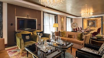 A spacious living room with a large flat-screen TV, a chandelier, and a variety of decorative items on a glass coffee table.