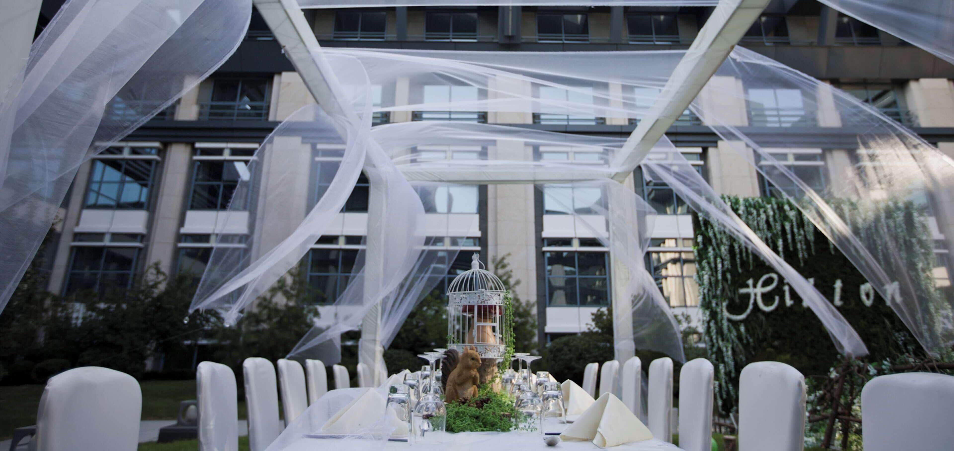 Una mesa dispuesta para una recepción de boda, con sillas blancas y un mantel blanco.