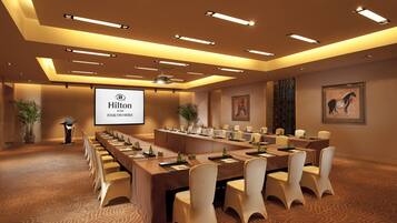 A conference room with a long table, chairs, a projector screen, and a potted plant.