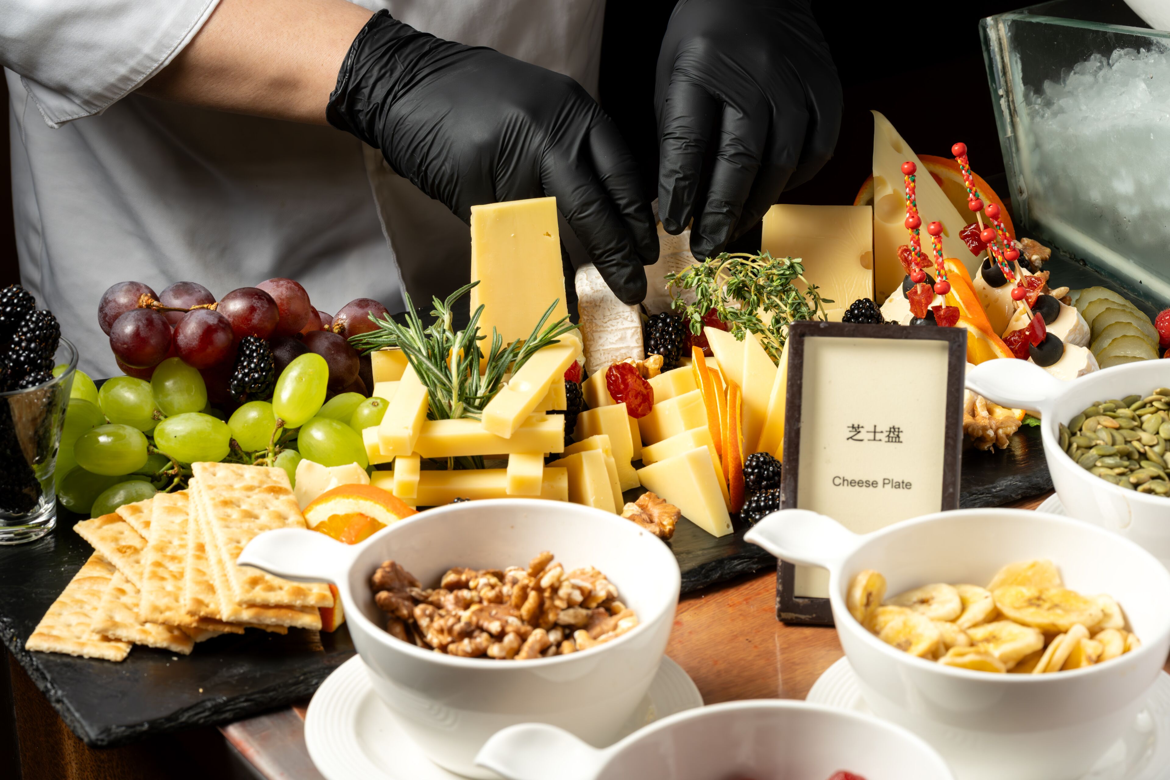 A variety of cheeses, fruits, and nuts arranged on a board, with a label reading 'Cheese Plate'.