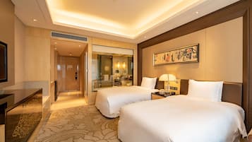 A hotel room with two beds, a desk, a mirror, a painting, and a bathroom visible through an open door.