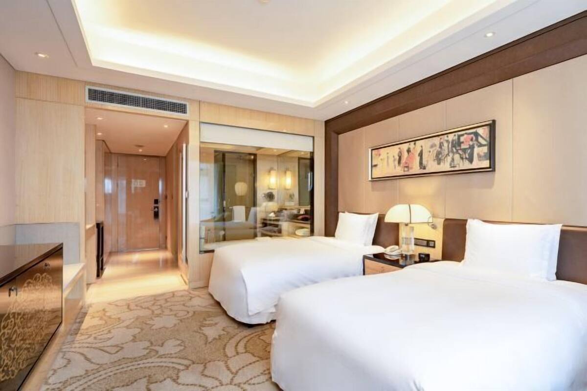 A hotel room with two beds, a desk, a chair, a mirror, and a painting on the wall.