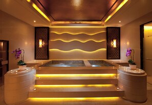 Un moderno espacio de spa con una bañera de hidromasaje central, dos paredes laterales con paneles decorativos e iluminación empotrada en el techo.