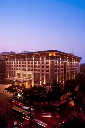 Un hotel grande de varios pisos con un llamativo letrero de "Hilton", que presenta un diseño arquitectónico moderno con techo plano e iluminación extensa.
